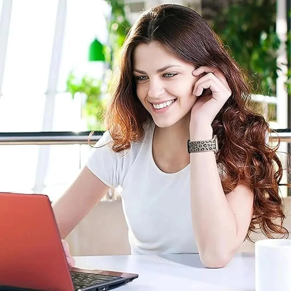 Woman with leopard print silicone engraved band using a laptop, showcasing style and comfort for Apple Watch.