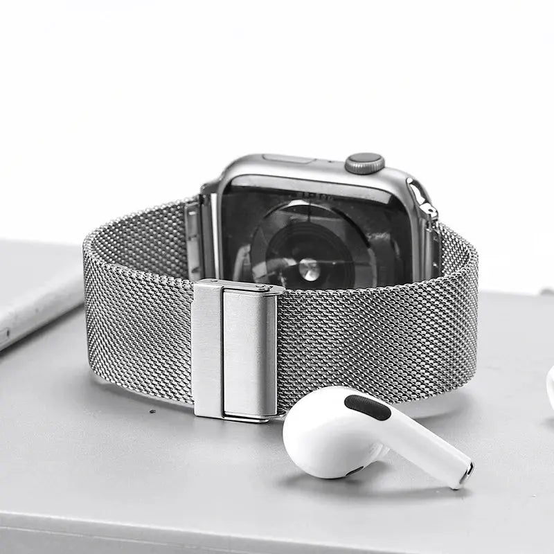 Milanese strap with secure clasp for Apple Watch displayed with AirPods, showcasing premium stainless steel mesh design.