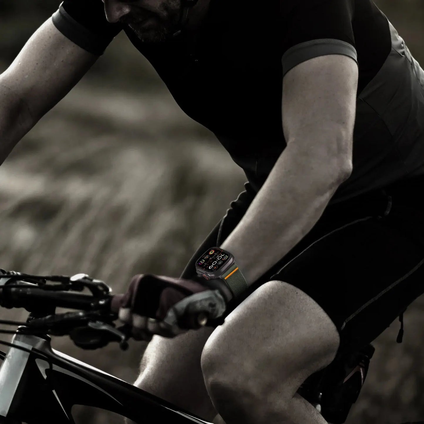 Man cycling with an Apple Watch fitted with a stretchy nylon loop band, showcasing durability and comfort during outdoor activities.