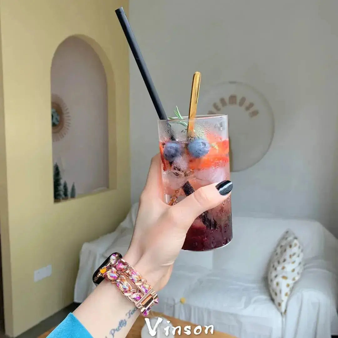 Woman holding a colorful drink with a black and gold stainless steel bracelet, showcasing a stylish accessory.
