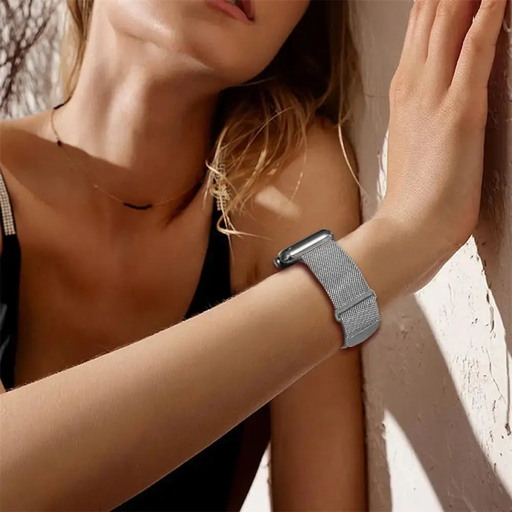 Woman wearing an exquisite stainless steel Milan Loop band on her Apple Watch against a stylish background.