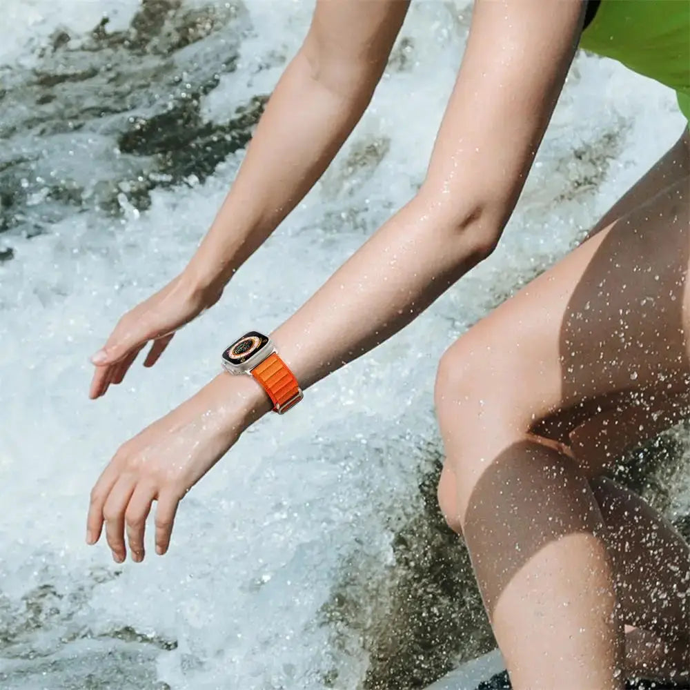 Person showing upgraded Alpine Loop watch while splashing in water, highlighting its rugged and stylish design.