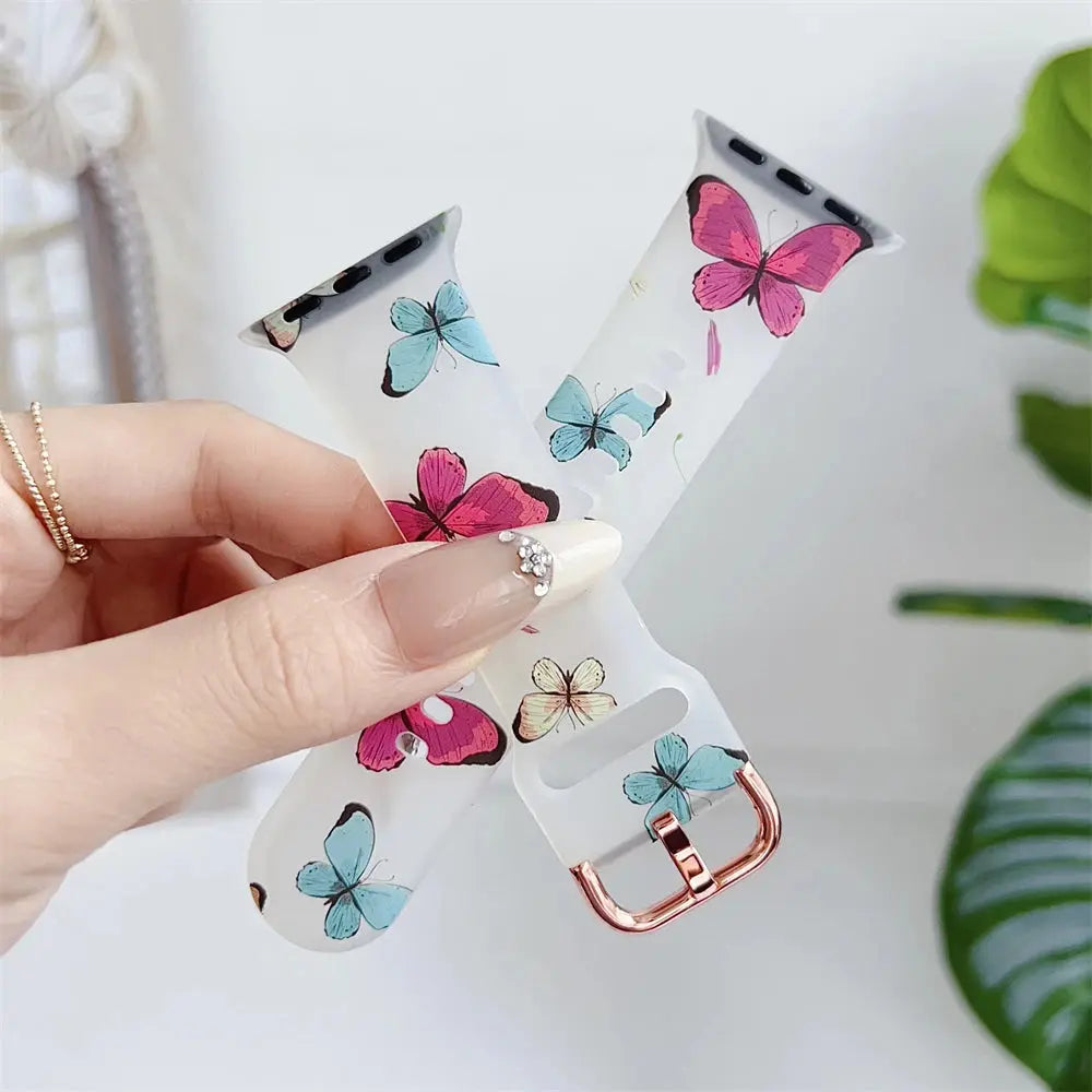 Clear silicone Apple Watch band with colorful flower and butterfly design held in hand.