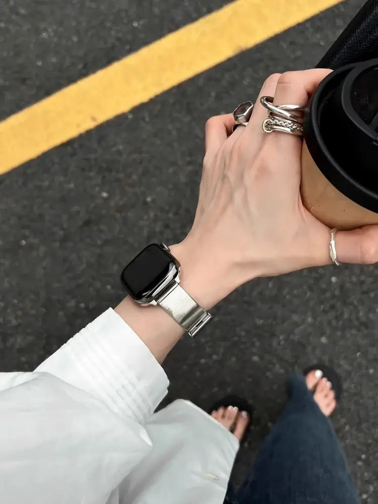 Glossy Stainless Steel Apple Watch Band – Slim Women’s Metal Strap (38–49mm) worn with a coffee cup in a stylish setting.