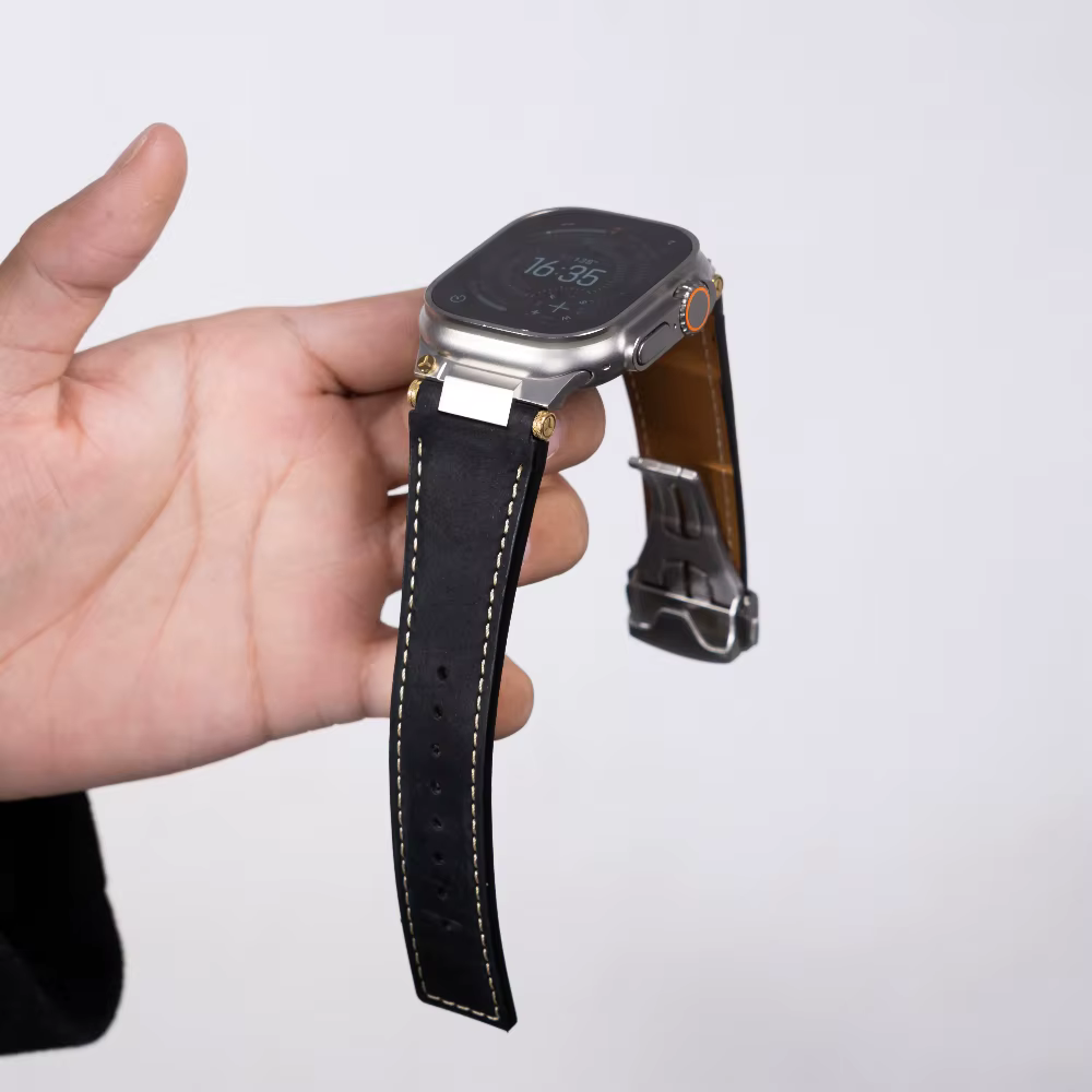Black leather Apple Watch strap held in hand, showing premium leather finish, reinforced stitching, and solid metal clasp for secure fit