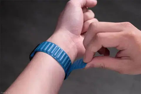 Person adjusting a blue leather link band on wrist, showcasing flexible fit for Apple Watch.