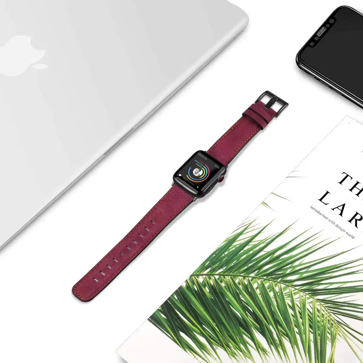 Retro style leather Apple Watch strap in burgundy, placed next to a laptop and greenery, showcasing luxury craftsmanship.