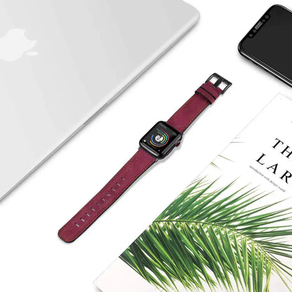 Retro style leather Apple Watch strap in burgundy, placed next to a laptop and greenery, showcasing luxury craftsmanship.