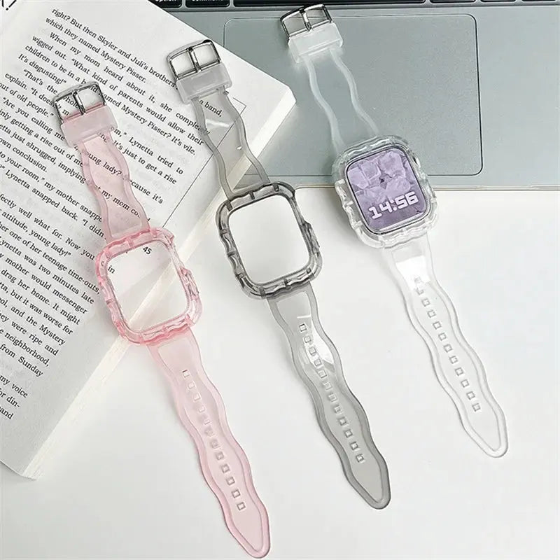 Crystal Clear Apple Watch strap and case set in pink, gray, and clear silicone on a desk next to a laptop.