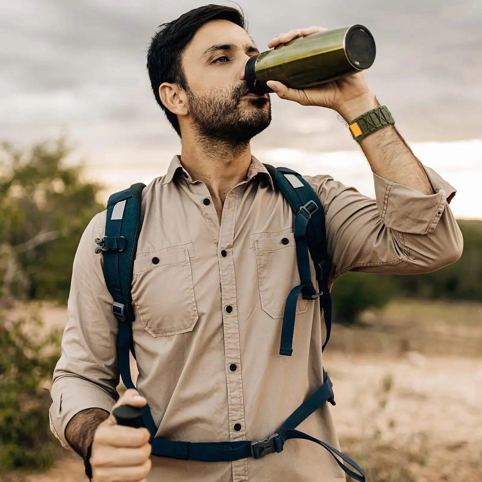 Man drinking from a bottle while wearing a tactical nylon loop band Apple Watch and outdoor gear.